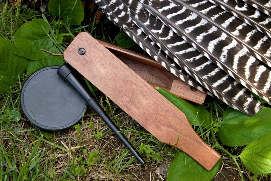 A closeup of a duck caller and feathers on the ground.