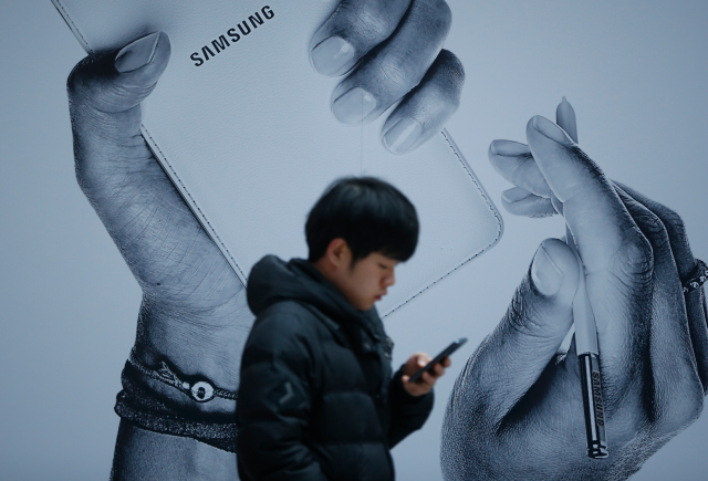 A passenger using his mobile phone walks past an advertisement promoting Samsung Electronics' Galaxy Note 3 at its exhibition hall at a railway station in Seoul November 25, 2013. REUTERS/Kim Hong-Ji