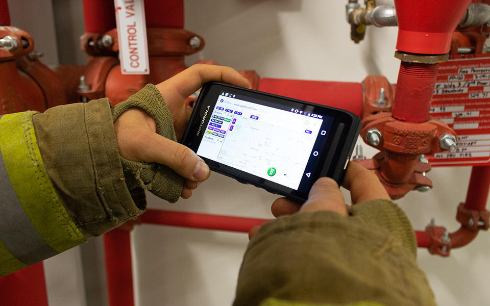 A person wearing a firefighter's coat holds a smartphone.