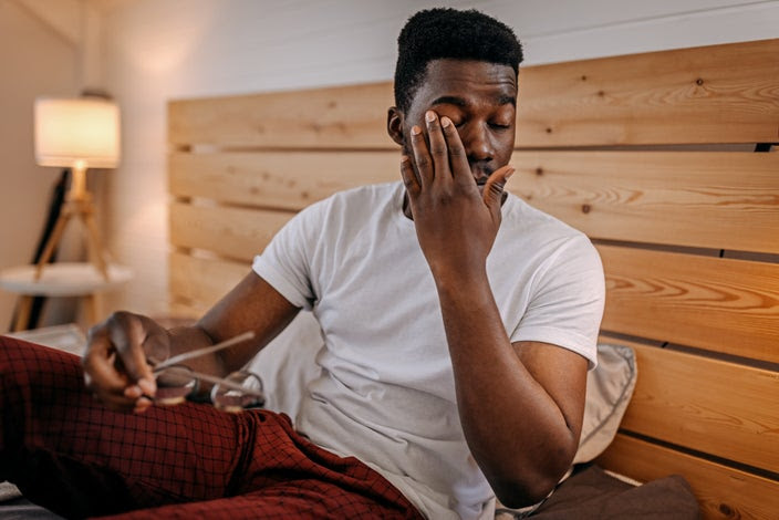 Man waking up in the morning and rubbing his eyes before he puts on his glasses.