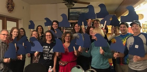 A group of Indivisible Yolo members hold blue wave signs at a general meeting