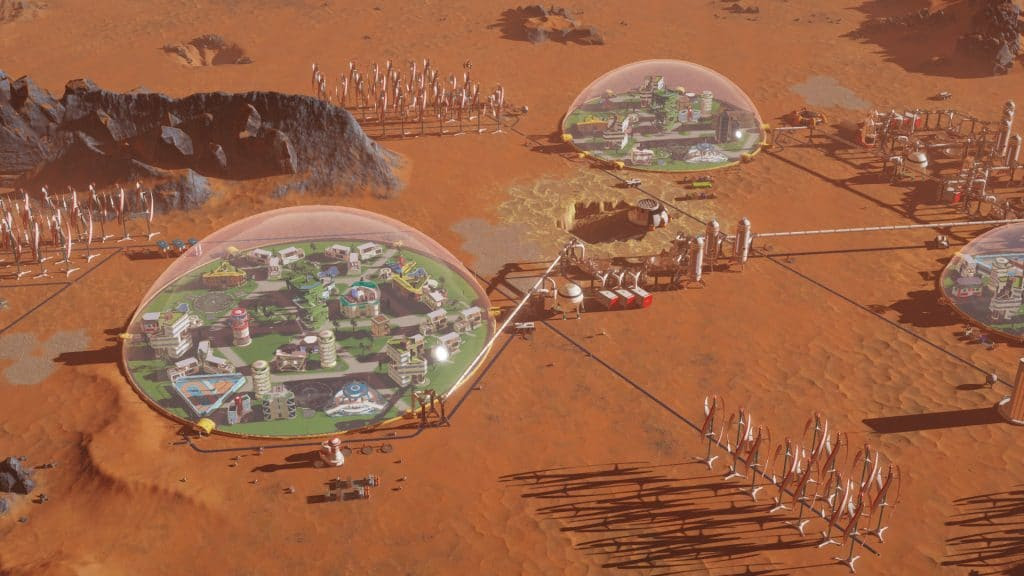 A screenshot of the game Surviving Mars, showing two transparent domes connected by a small passage, as well as some other sciencey-looking devices, on a desertic red surface.