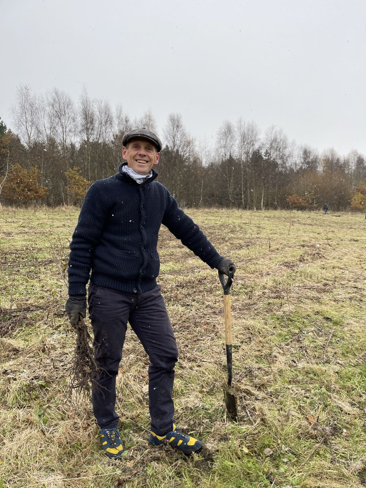 Councillor Scott Cunliffe holding a shovel and trees at the tree planting site