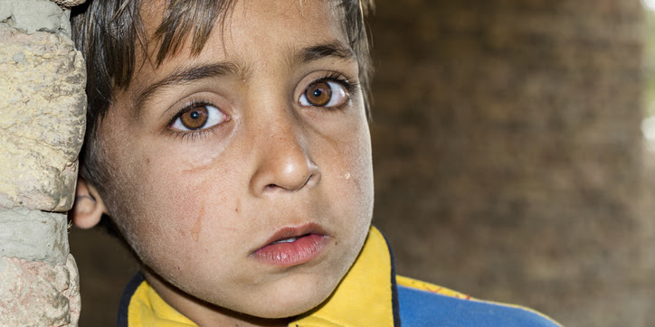 Terrified child looks out from refugee camp.