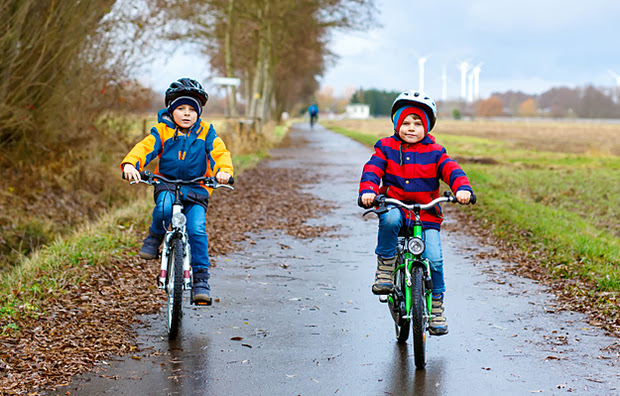Two young boys riding bicycles on a paved path.