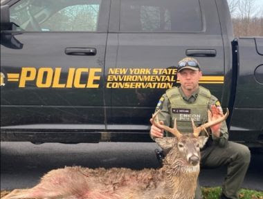 ECO holding deceased buck by antlers next to ECO truck