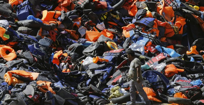 Un hombre pasa junto a una montaña de botes desinflados y chalecos salvavidas dejados por los refugiados tras su llegada a la isla griega de Lesbos. REUTERS