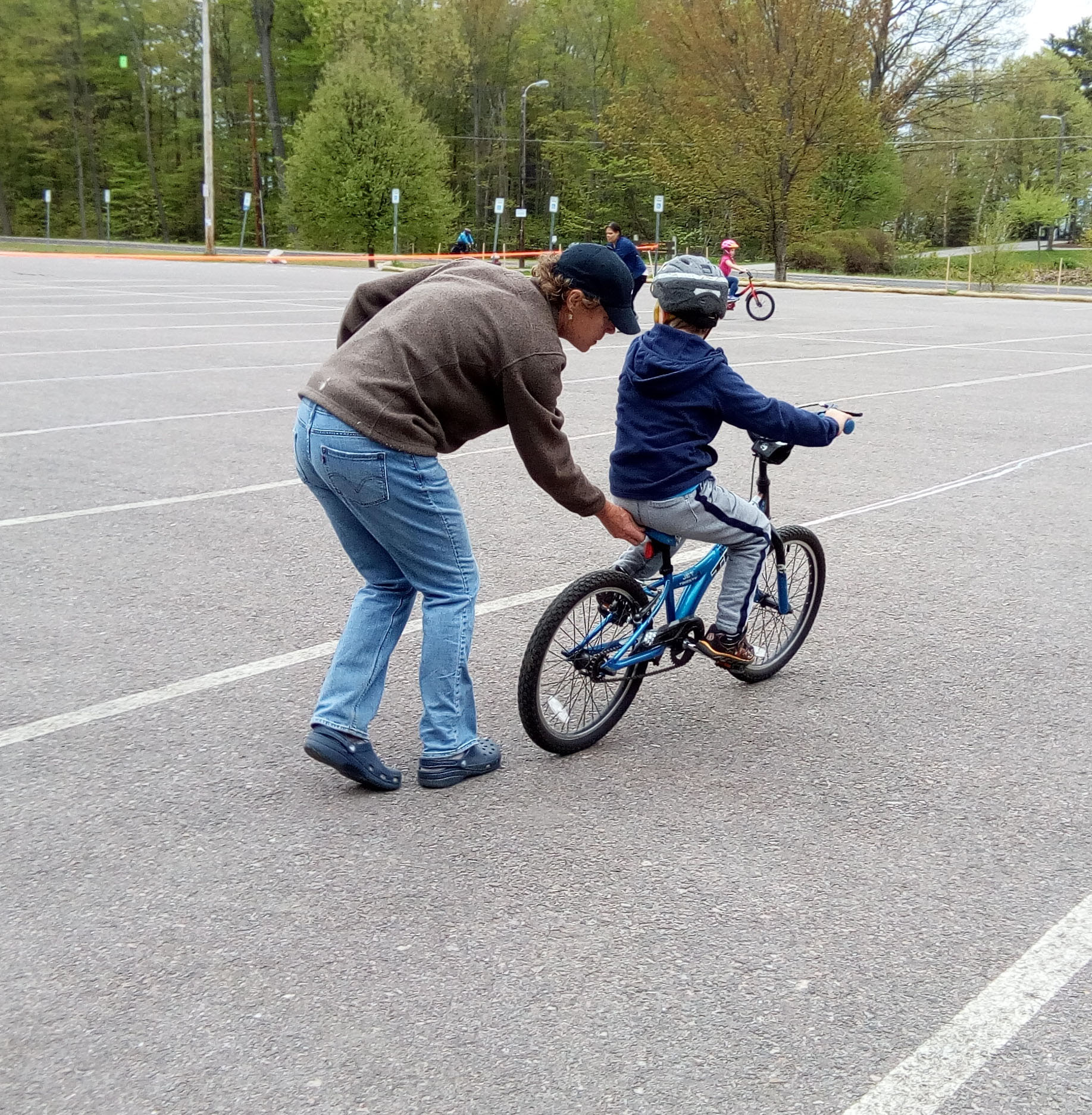 Volunteer holding back of child's bike as they learn to ride

without training wheels for the first time in an empty parking lot