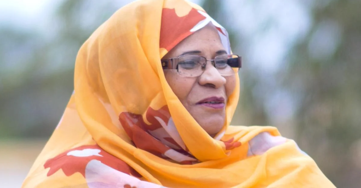 A photo of Zeinebou Taleb Moussa from the shoulders up. She is wearing a light orange headscarf decorated with large dark orange flowers. She is also wearing glasses. 