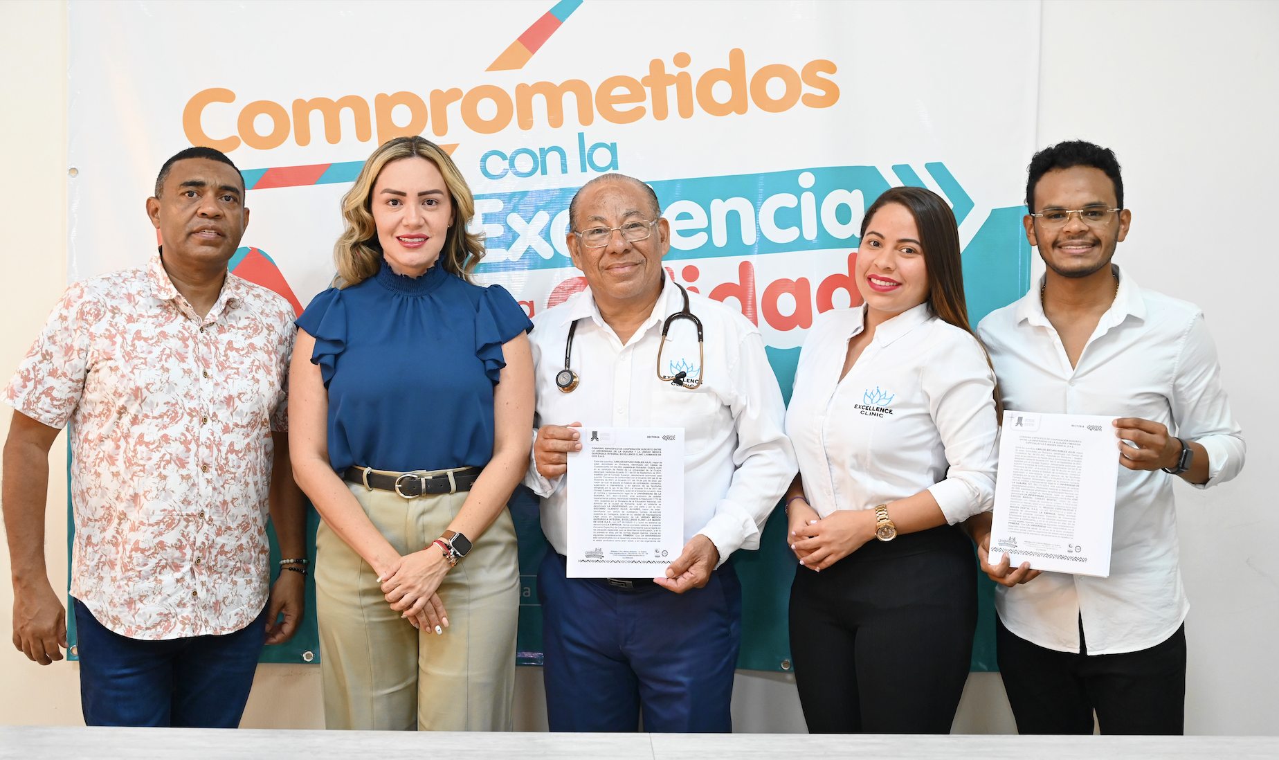 Grupo de personas posando en una sala, con dos convenios en mano.