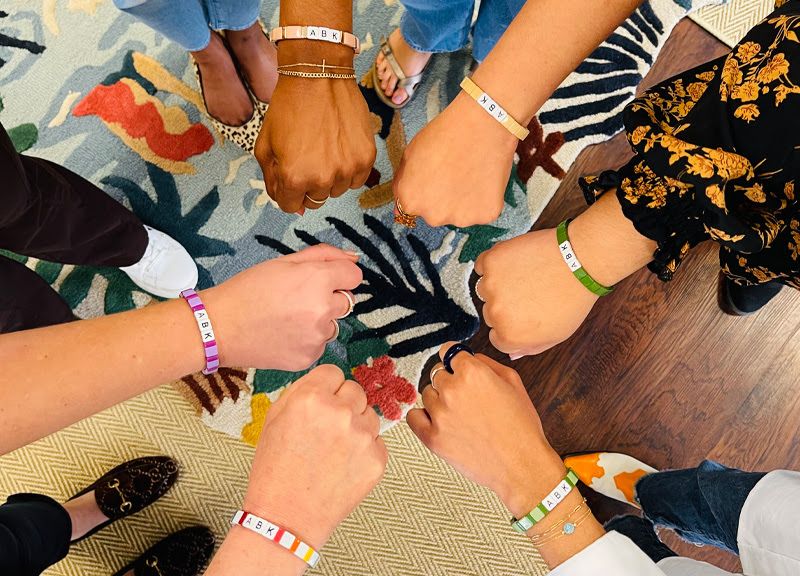 Hands (wearing awkward, brave, and kind bracelets) in a circle