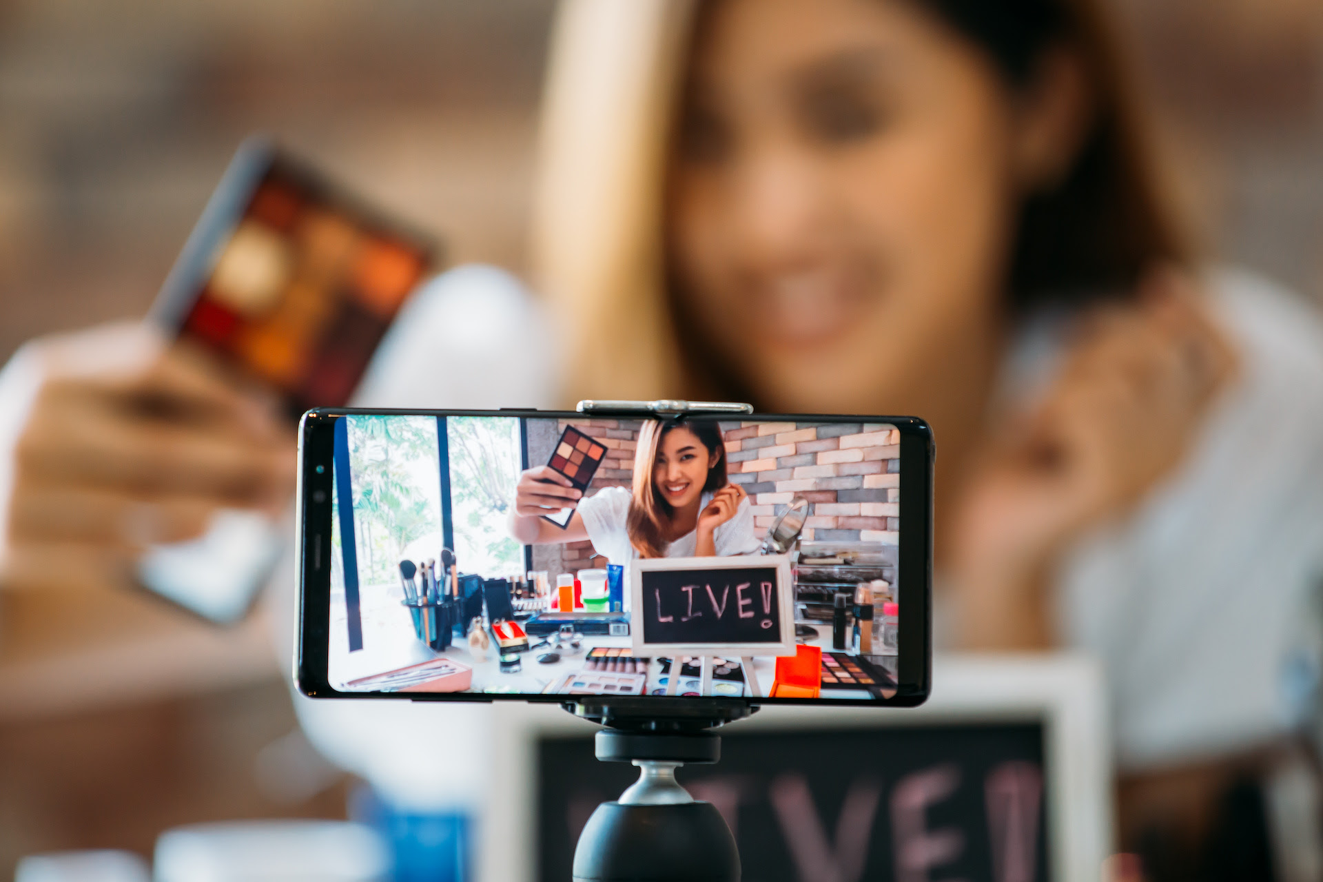アイシャドウを手にして見せながらスマホで撮影している女性・スマホにその様子が映っている