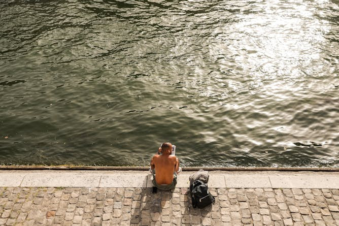 A person sits shirtless on the bank of the Seine in Paris.