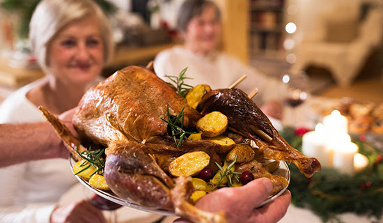 Close up of a roasted turkey being brought to the dinner table on a serving tray.