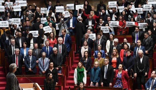 French lawmakers standing in Parliament, with many holding signs.