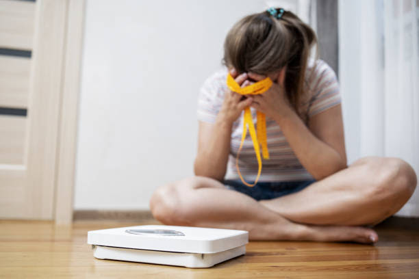 White scale and depression, upset and sad woman with measuring tape on wooden floor White scale and depression, upset and sad woman with measuring tape on wooden floor. slim fit healthy ladies stock pictures, royalty-free photos & images