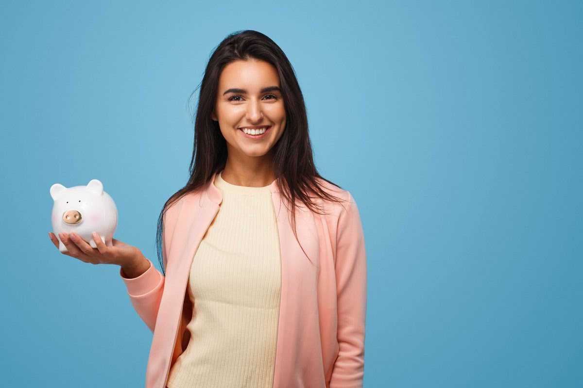 A young woman smiling and holding a piggy bank