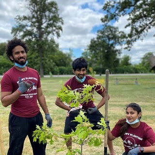 Two men and a woman wearing Happy Little T-shirts pose with a tree they are planting at Belle Isle in Detroit