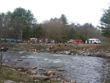 wide angle of a creek with various rescue crews pulling a man and his car out of the creek