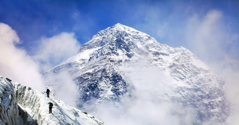 Three climbers walking up snowy mountain with the Mount Everest peak in the background