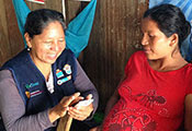 Health worker enters data on mobile device while seated pregnant patient looks on